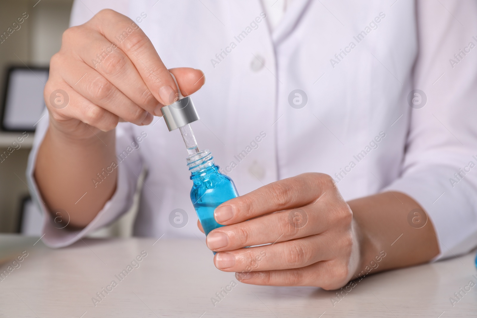 Photo of Dermatologist developing cosmetic product at white table indoors, closeup