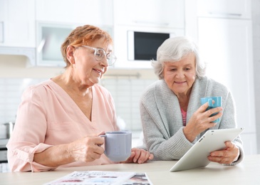 Photo of Elderly women using tablet PC at table in kitchen