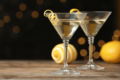 Photo of Glasses of Lemon Drop Martini cocktail with zest on wooden table against blurred background. Space for text