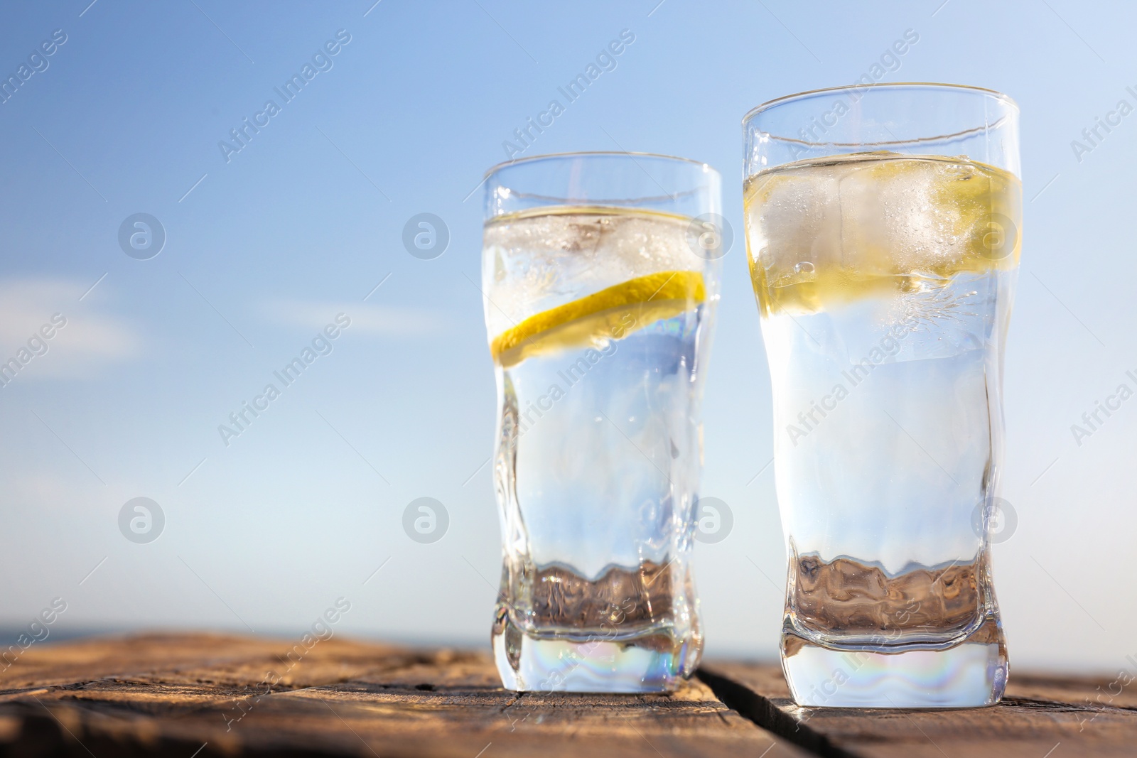 Photo of Wooden table with glasses of refreshing lemon drink on hot summer day outdoors, space for text