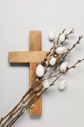 Wooden cross, painted Easter eggs and willow branches on light grey background, top view