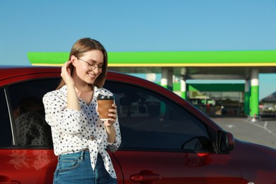 Photo of Beautiful young woman with coffee near car at gas station