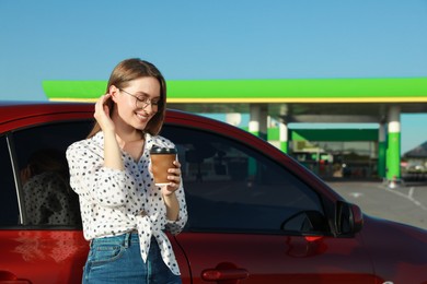 Beautiful young woman with coffee near car at gas station