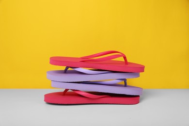 Photo of Stack of flip flops on white table against yellow background