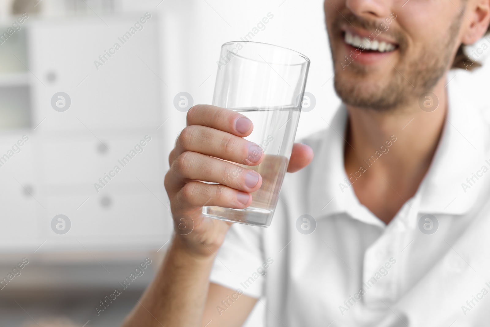 Photo of Young man holding glass of clean water indoors, closeup. Space for text