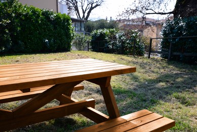 Photo of Empty wooden picnic table with benches in backyard on sunny day