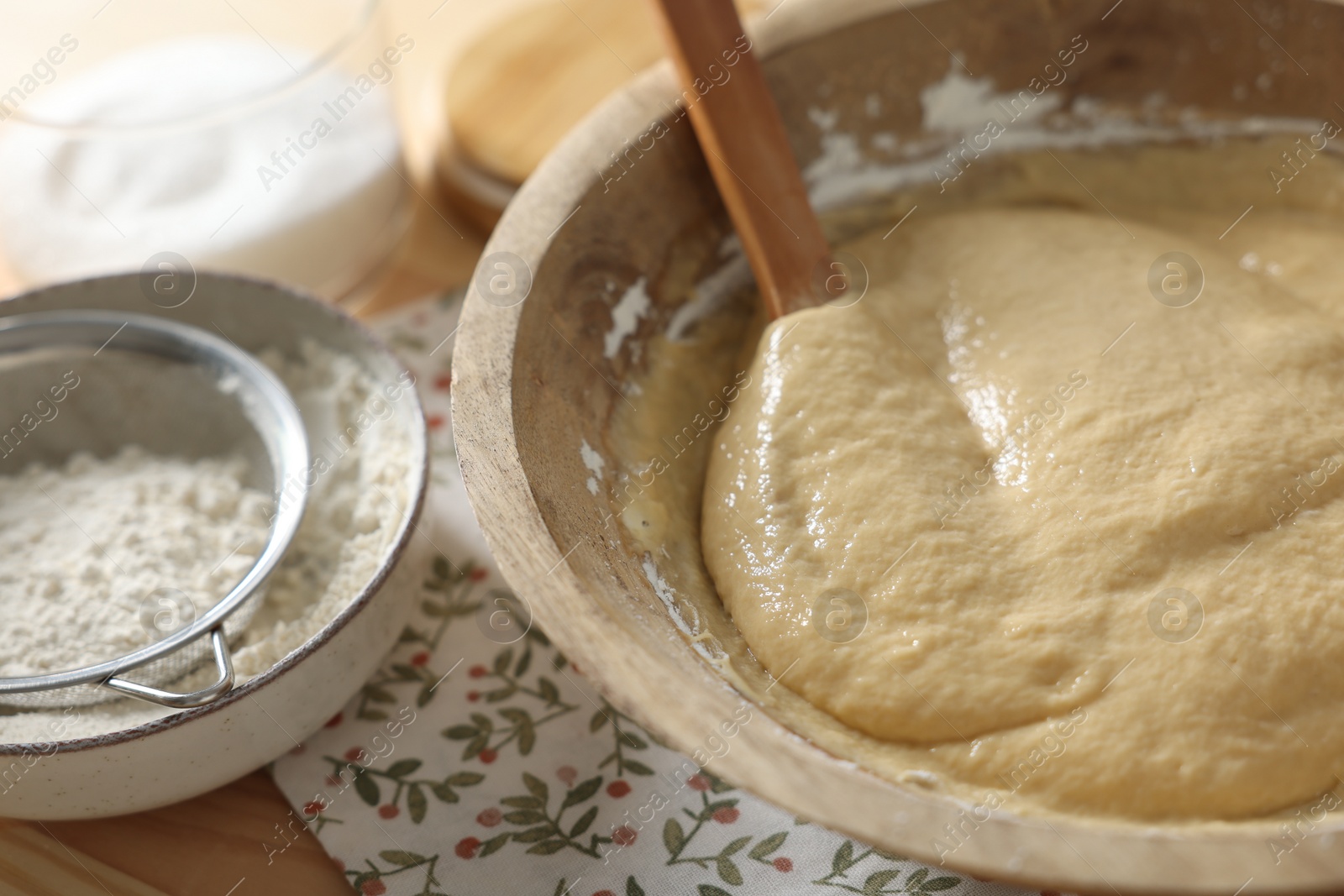 Photo of Raw dough in bowl on wooden table, closeup