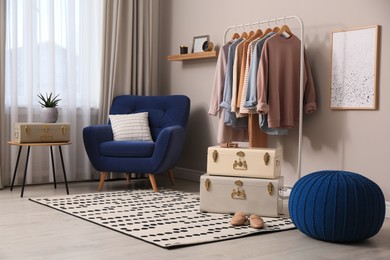 Stylish room interior with comfortable armchair, clothes and storage trunks