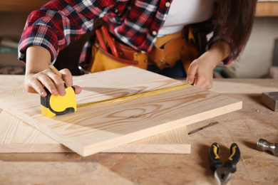 Photo of Female carpenter measuring wooden board in workshop, closeup