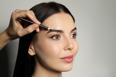 Photo of Artist correcting woman's eyebrow shape with pencil on grey background, closeup