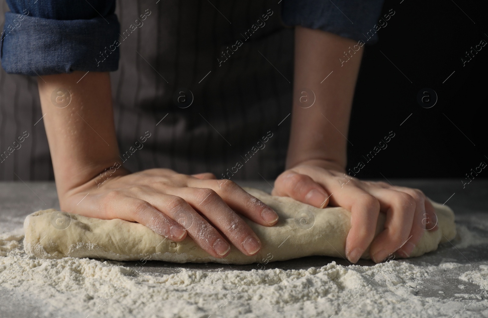 Photo of Making bread. Woman kneading dough at table on dark background, closeup