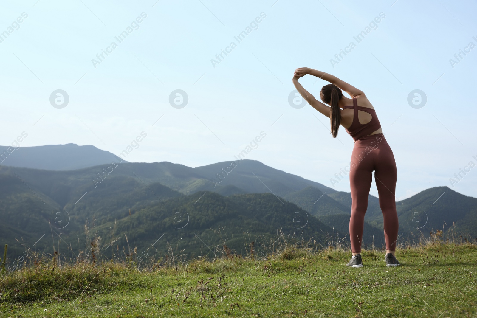 Photo of Woman doing morning exercise in mountains, back view. Space for text