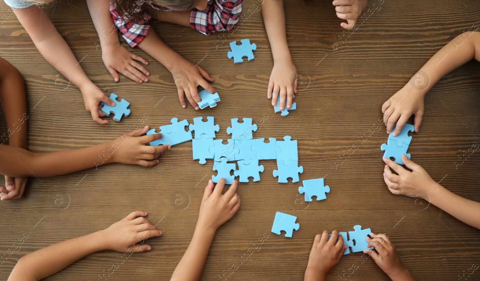 Photo of Top view of little children playing puzzle together at table, focus on hands. Unity concept