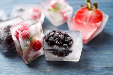 Ice cubes with different berries and mint on blue wooden table, closeup