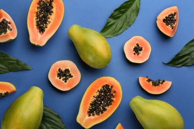 Fresh ripe papaya fruits with green leaves on blue background, flat lay