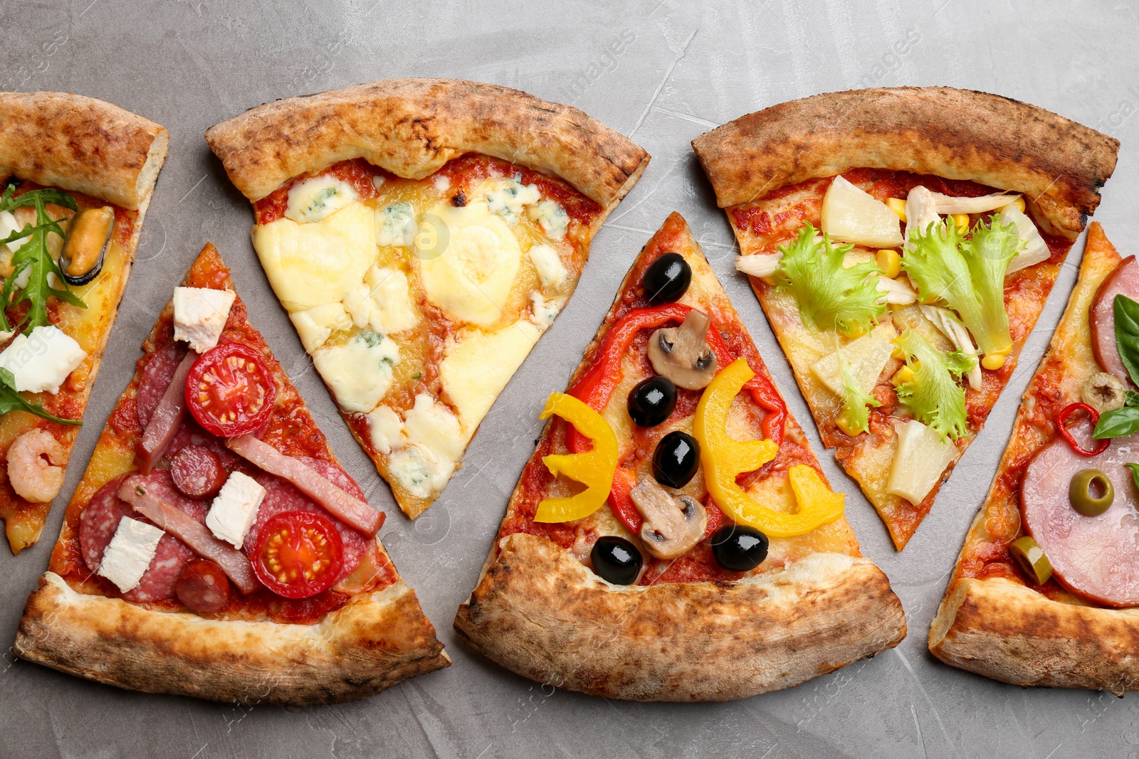 Photo of Slices of different delicious pizzas on grey table, flat lay