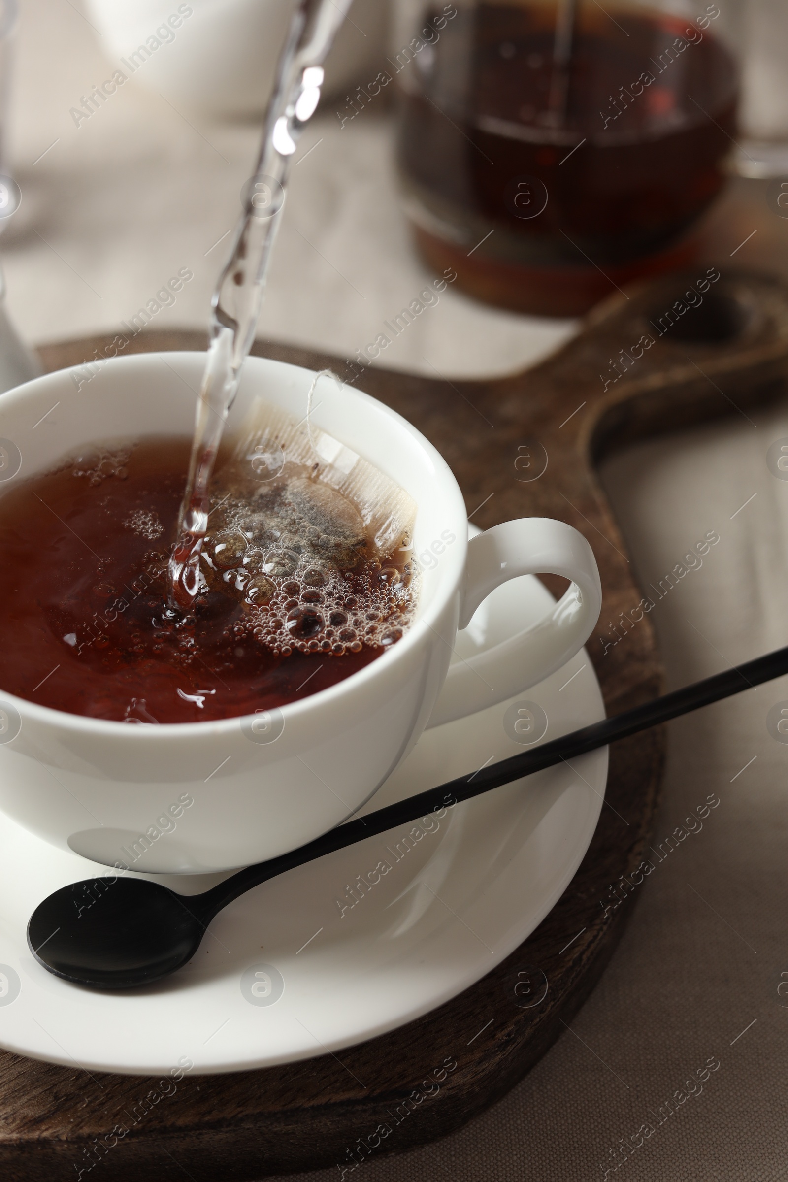 Photo of Pouring hot water into cup with tea bag on light table, closeup