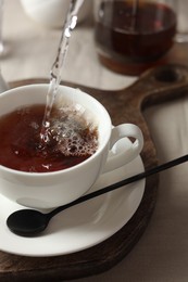 Photo of Pouring hot water into cup with tea bag on light table, closeup