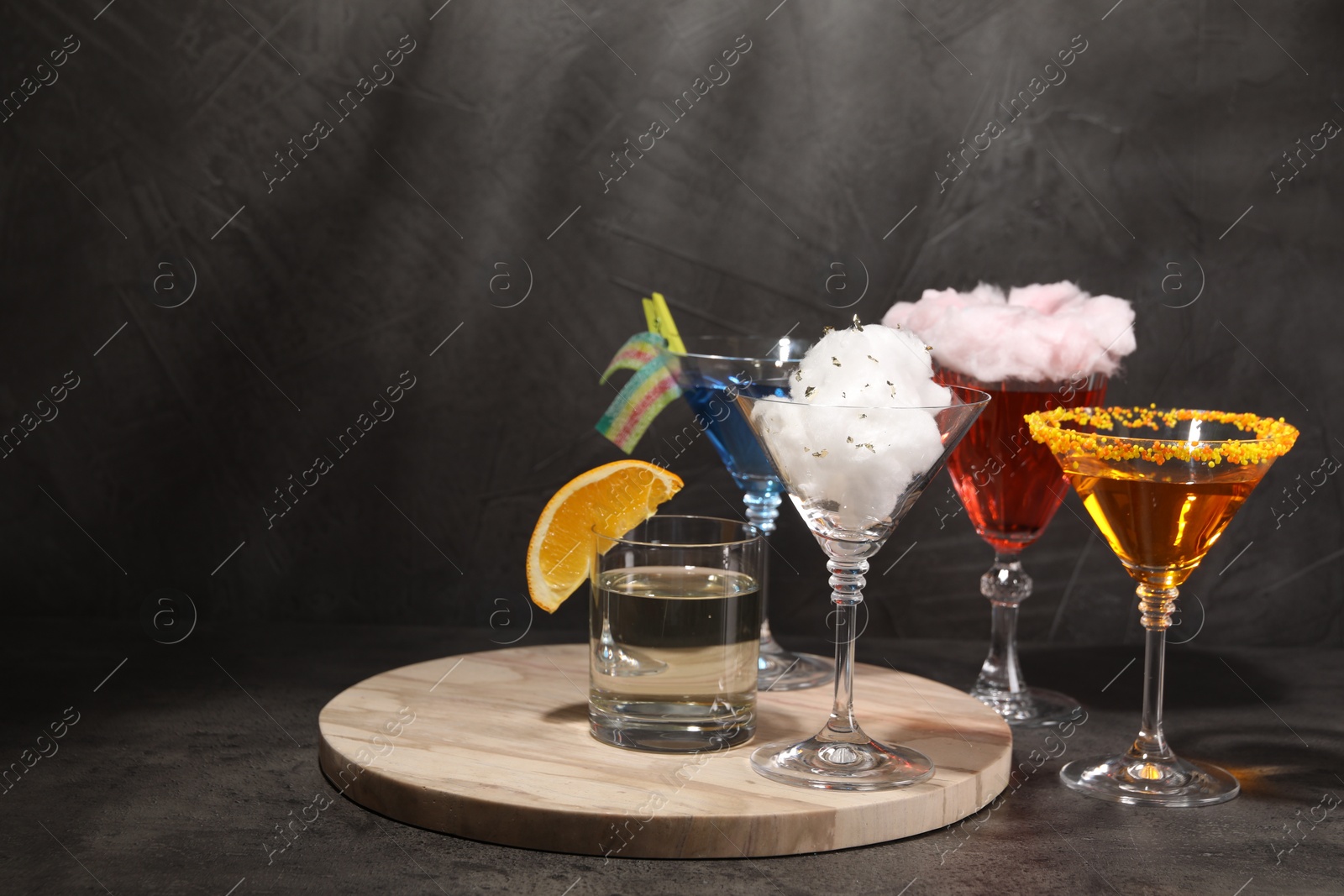 Photo of Tasty cotton candy cocktail and other alcoholic drinks in glasses on gray textured table, space for text