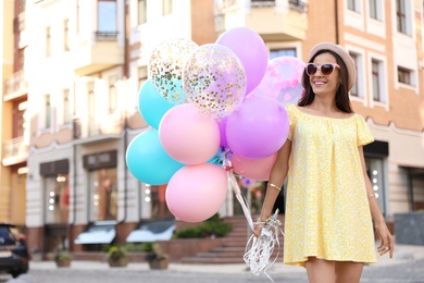 Photo of Beautiful young woman with color balloons on city street