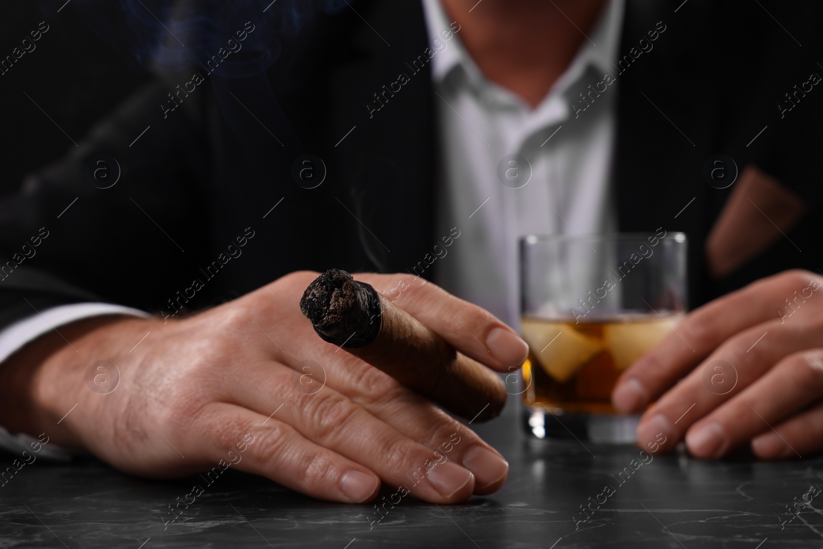 Photo of Man with glass of whiskey smoking cigar at dark marble table, closeup