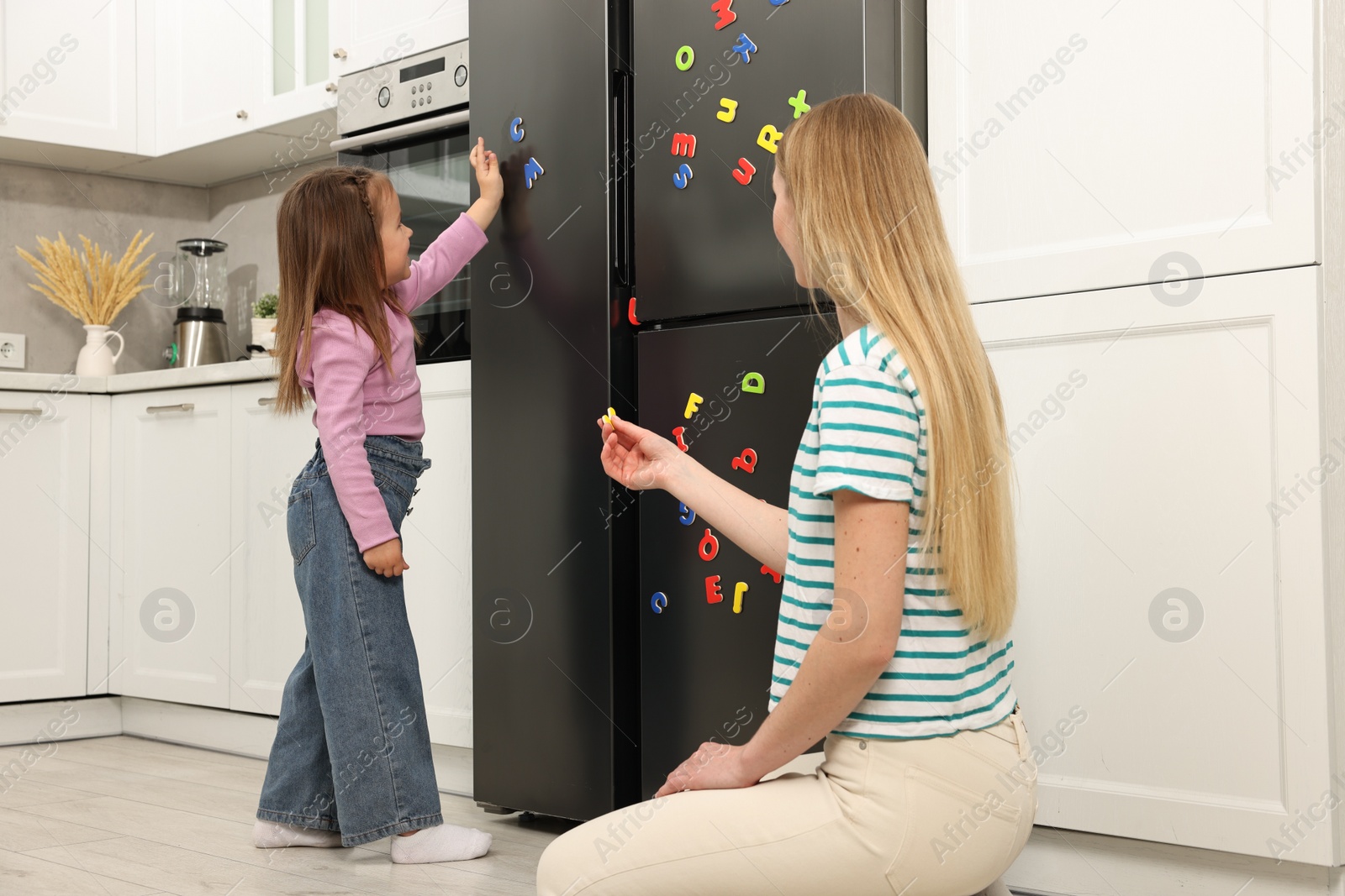 Photo of Mom and daughter putting magnetic letters on fridge at home. Learning alphabet