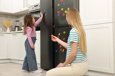Photo of Mom and daughter putting magnetic letters on fridge at home. Learning alphabet