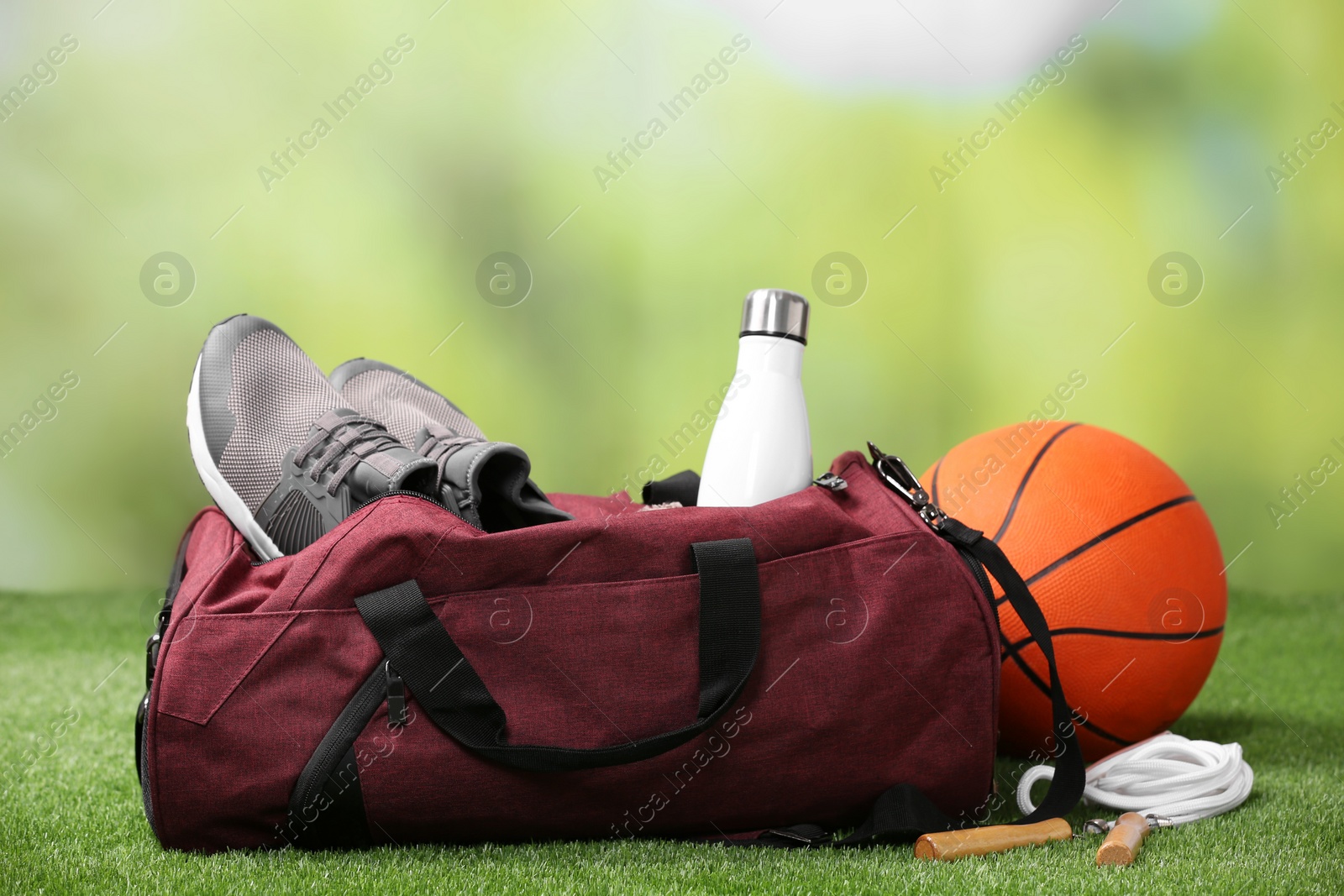 Photo of Bag and different sports equipment on grass against blurred background