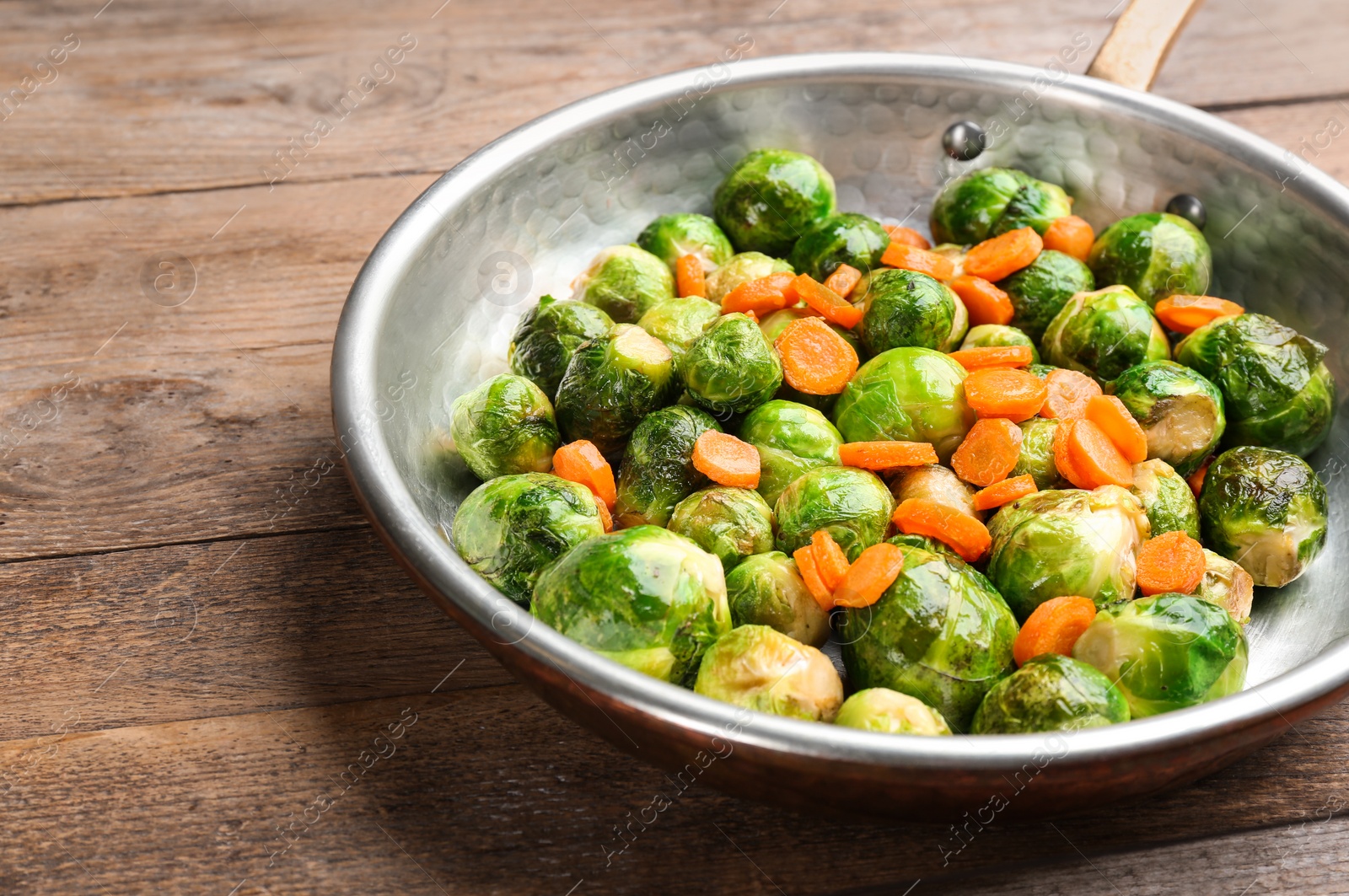 Photo of Roasted Brussels sprouts with carrot in frying pan on wooden table
