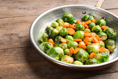Roasted Brussels sprouts with carrot in frying pan on wooden table