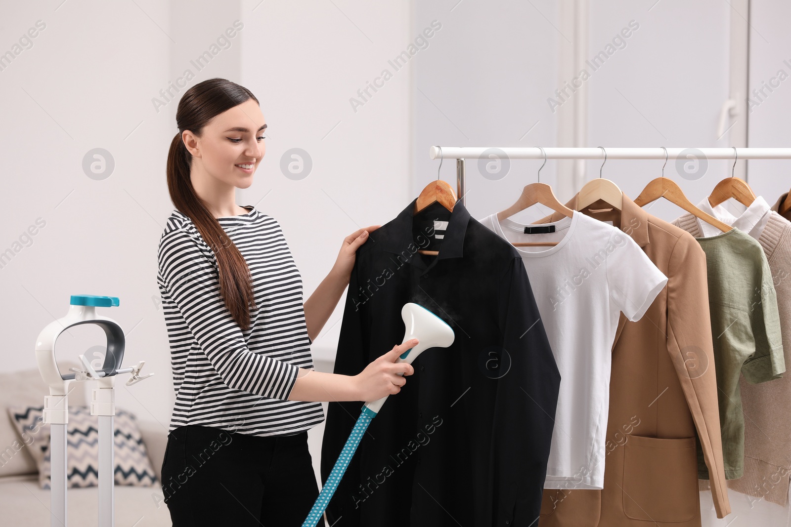 Photo of Woman steaming black shirt on hanger at home