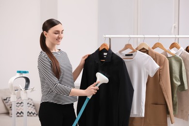 Woman steaming black shirt on hanger at home