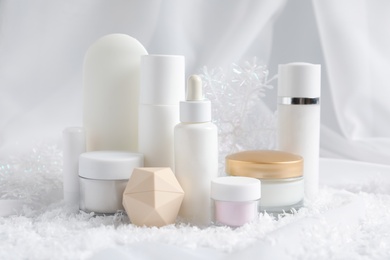 Photo of Set of cosmetic products and decorative snow on white fabric. Winter care