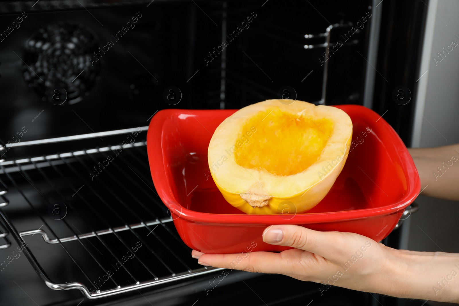 Photo of Woman putting half of fresh spaghetti squash into oven, closeup