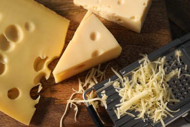 Grated, cut cheese and grater on wooden table, flat lay