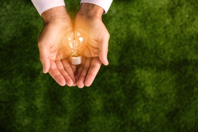 Photo of Man holding lamp bulb against green background, top view. Space for text