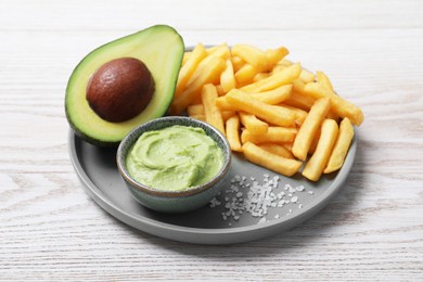 Photo of Plate with french fries, guacamole dip and avocado served on white wooden table