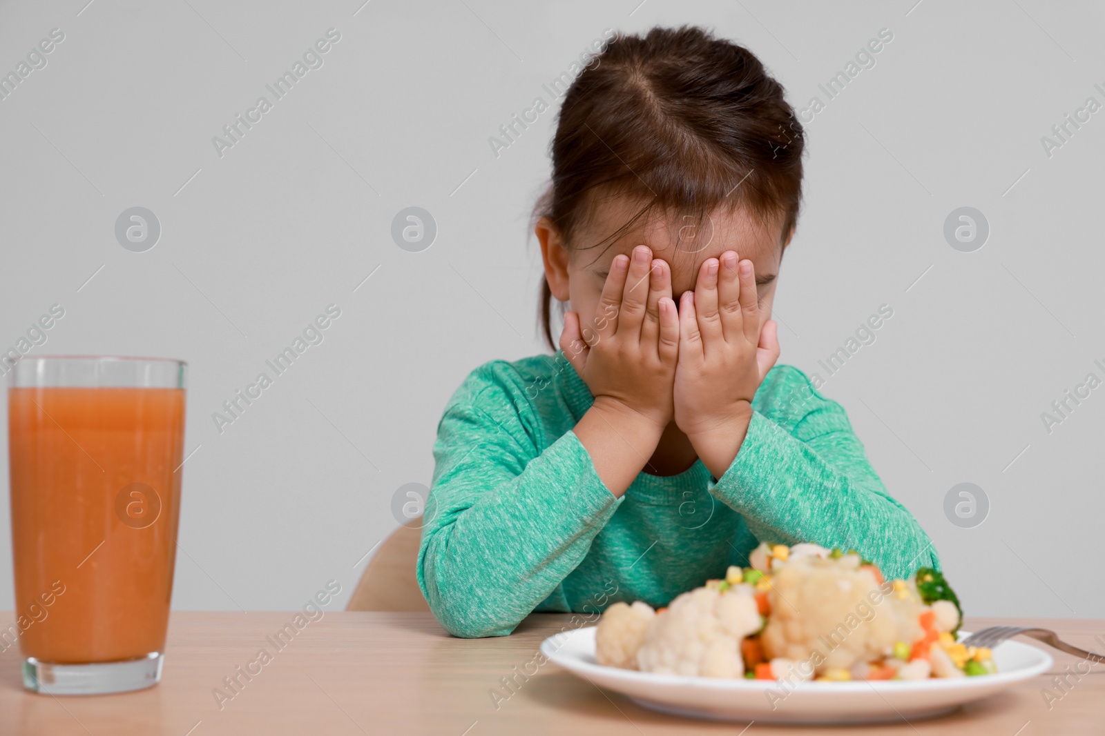 Photo of Cute little girl crying and refusing to eat vegetable salad at table on grey background