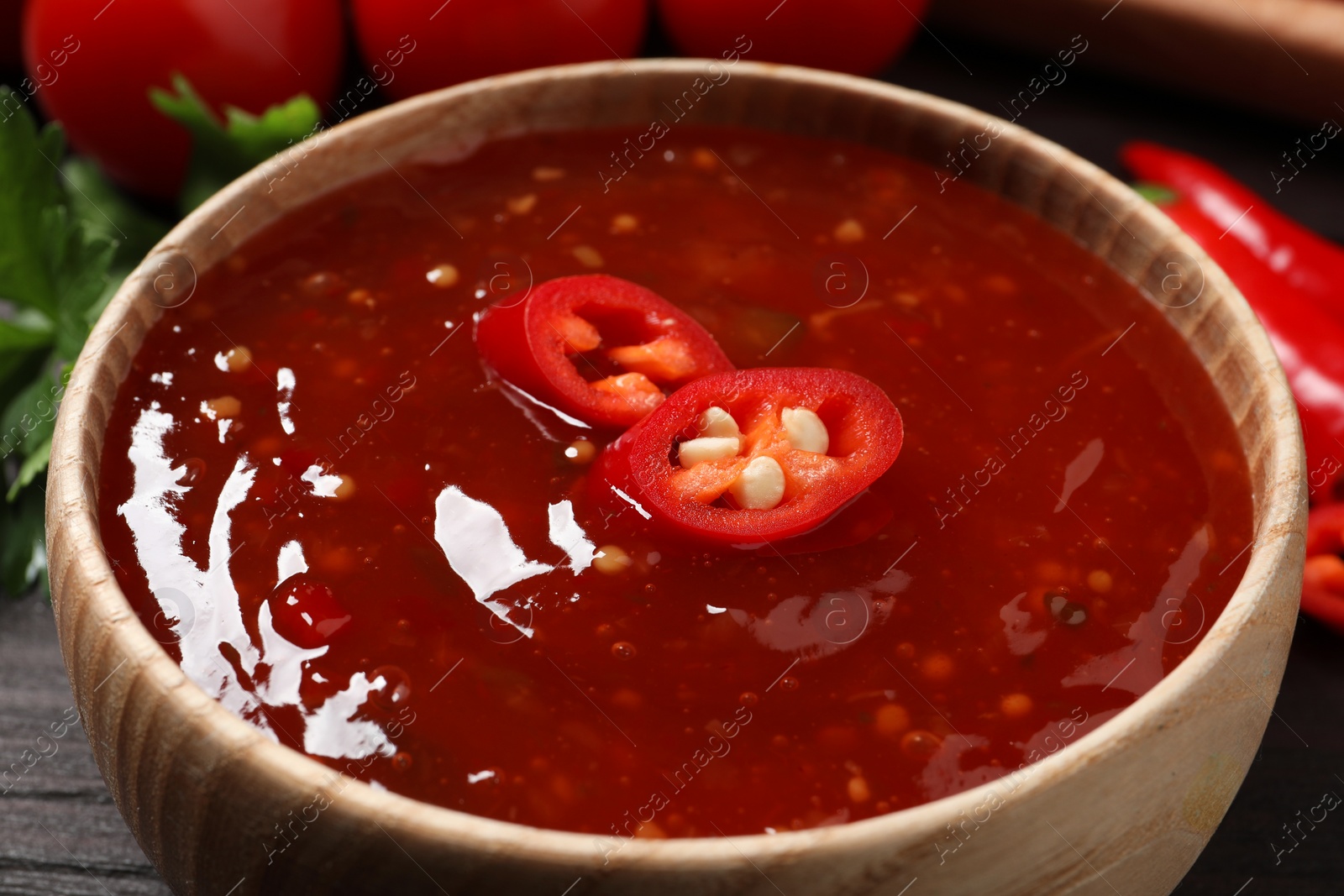 Photo of Spicy chili sauce in bowl on wooden table, closeup