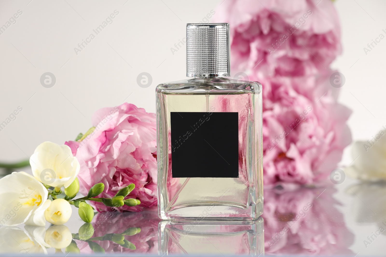 Photo of Bottle of luxury perfume and floral decor on mirror surface against white background, closeup