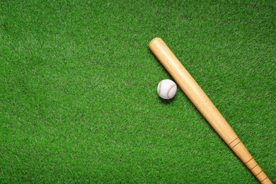 Photo of Wooden baseball bat and ball on green grass, flat lay. Space for text