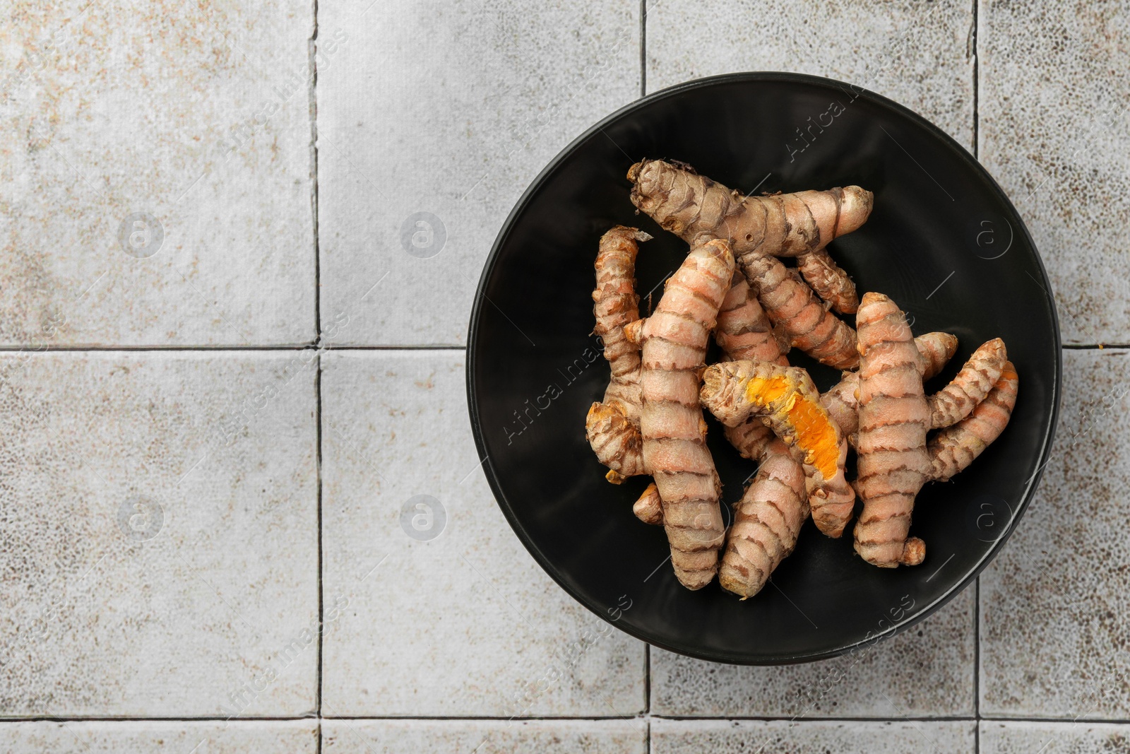 Photo of Bowl with raw turmeric roots on white tiled table, top view. Space for text