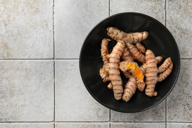 Bowl with raw turmeric roots on white tiled table, top view. Space for text