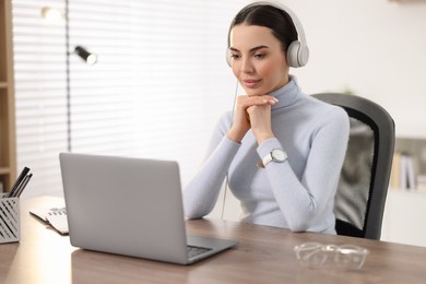 Young woman in headphones watching webinar at table in office