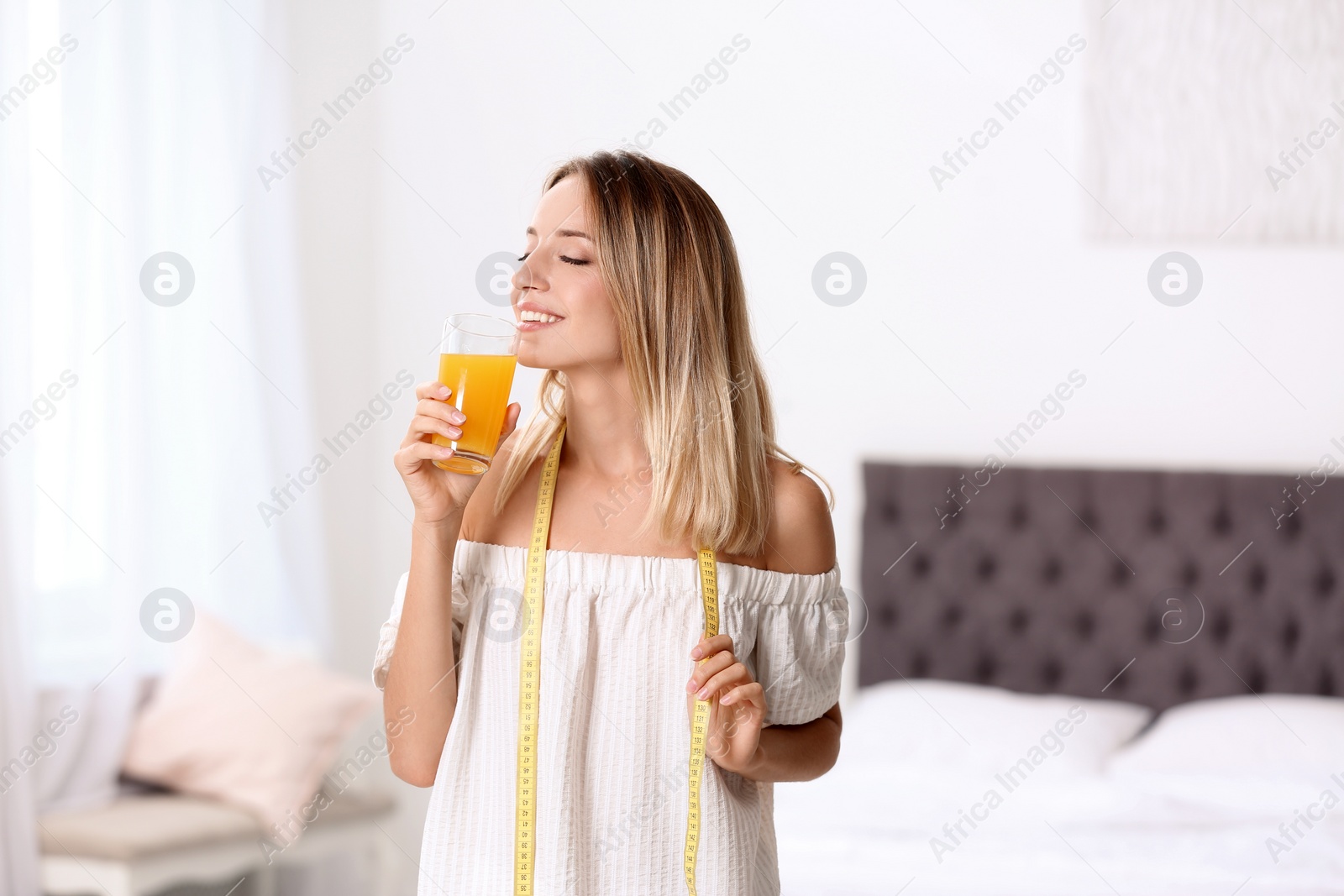 Photo of Happy slim woman with measuring tape and glass of juice at home. Positive weight loss diet results