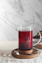 Delicious hibiscus tea in teapot and sugar cubes on table. Space for text