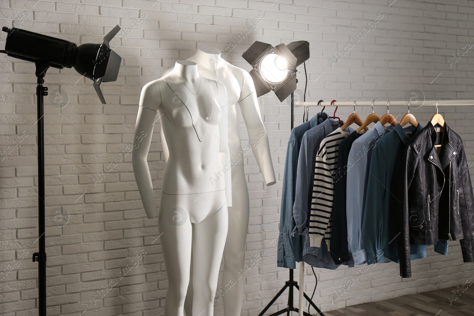 Photo of Ghost mannequins, clothes and professional lighting equipment in modern studio. Fashion photography