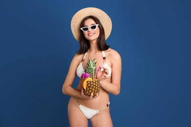 Beautiful woman in stylish bikini holding tropical cocktail on blue background