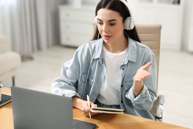 Young woman in headphones using video chat during webinar at table in room