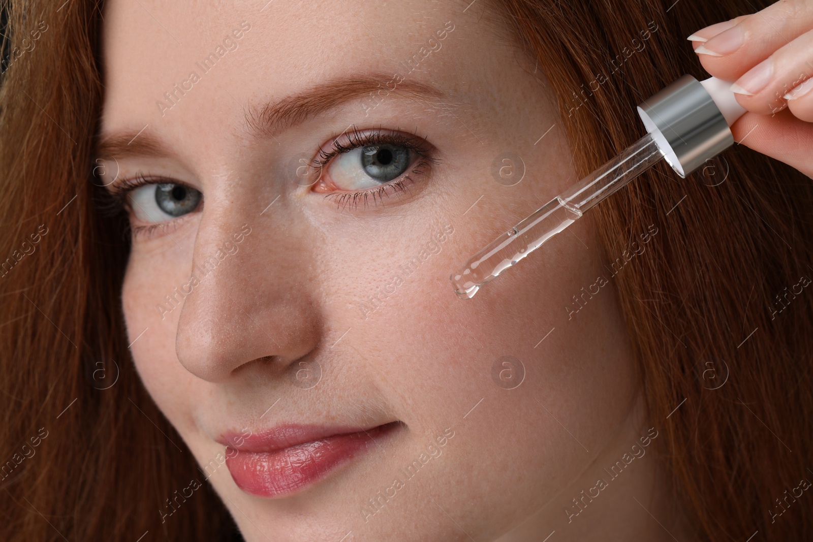 Photo of Beautiful woman with freckles applying cosmetic serum onto her face, closeup